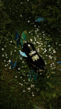 a bottle laying in the grass with butterflies flying around it